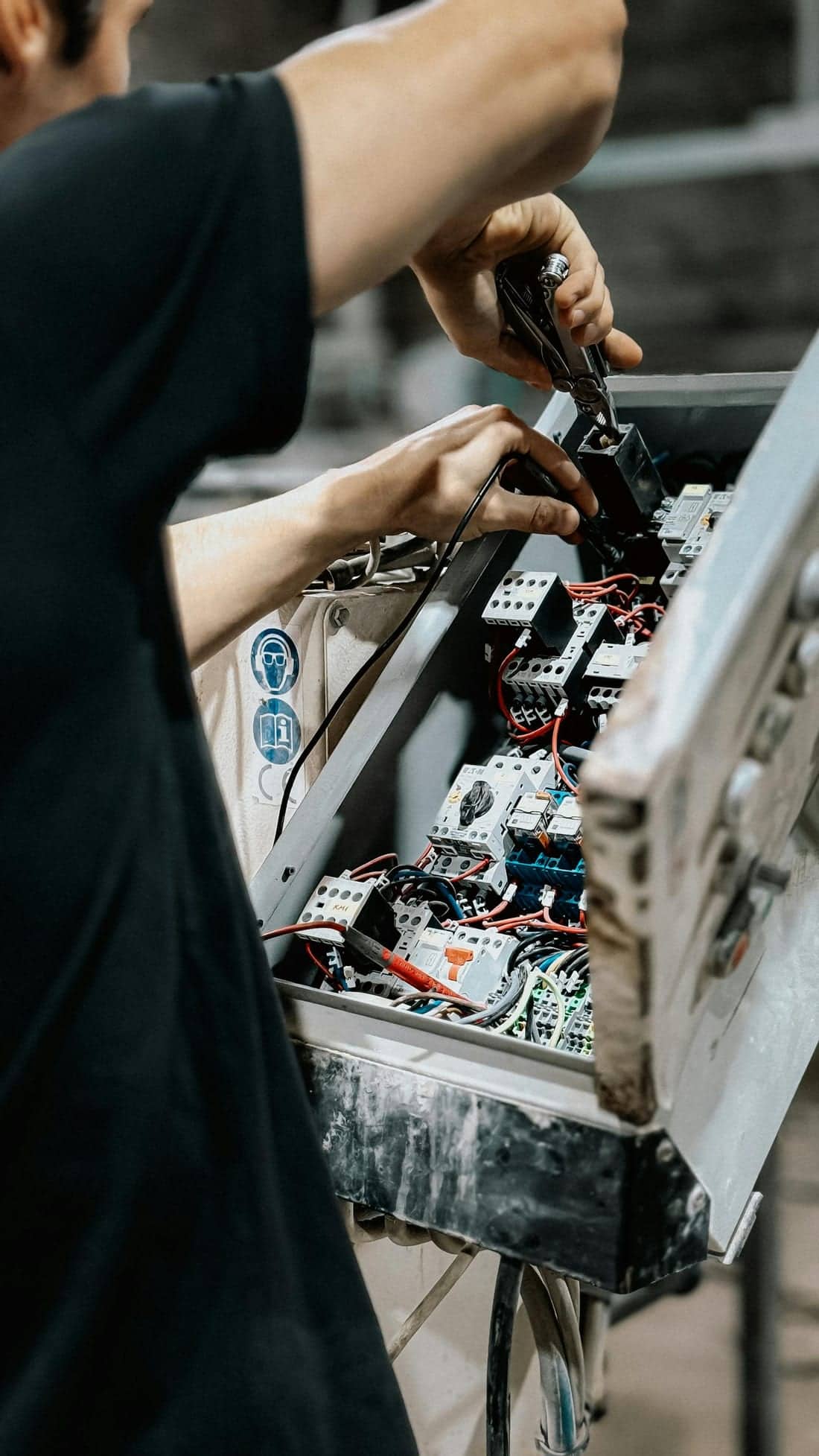 Technician adjusting wires inside an electrical control panel - the kind of overloaded shop panel typical in Nirala Bazaar that we rebuild during a wiring upgrade or AMC visit