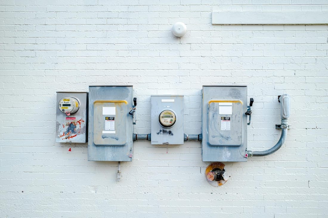 Electrical distribution boxes and power meters mounted on a clean white brick wall - the utility entry on a newly built Paithan Road property