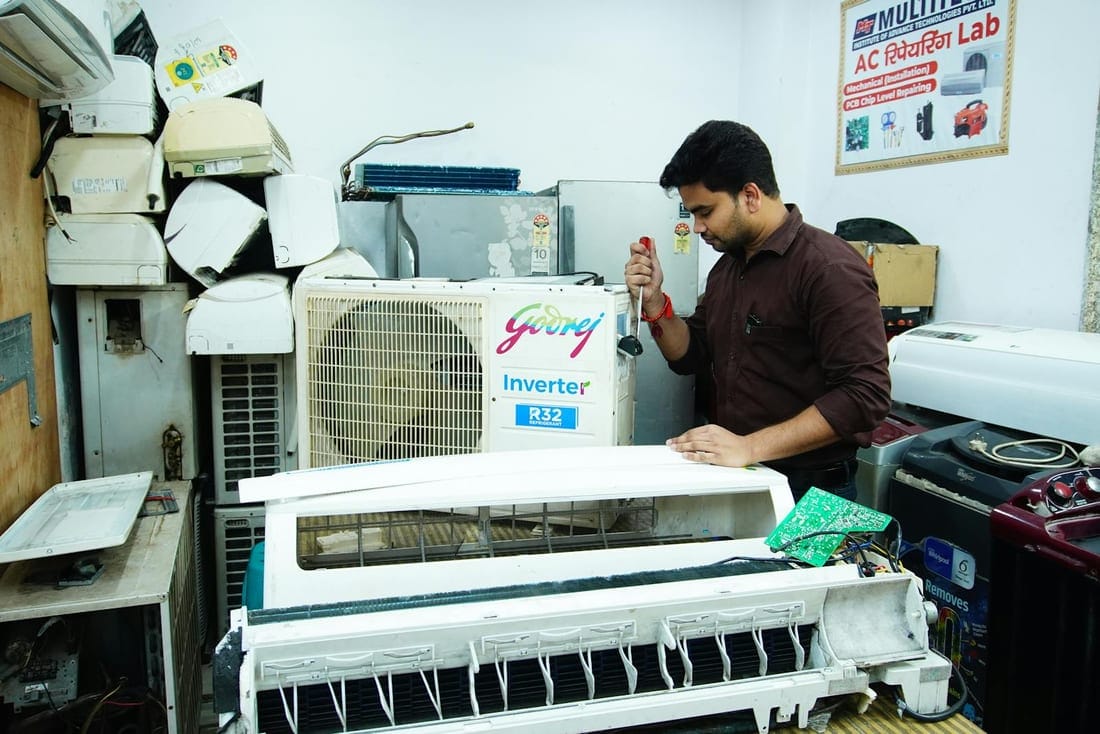 Technician opening a split AC indoor unit on a workbench during a repair - the diagnostic work that follows voltage-related compressor faults