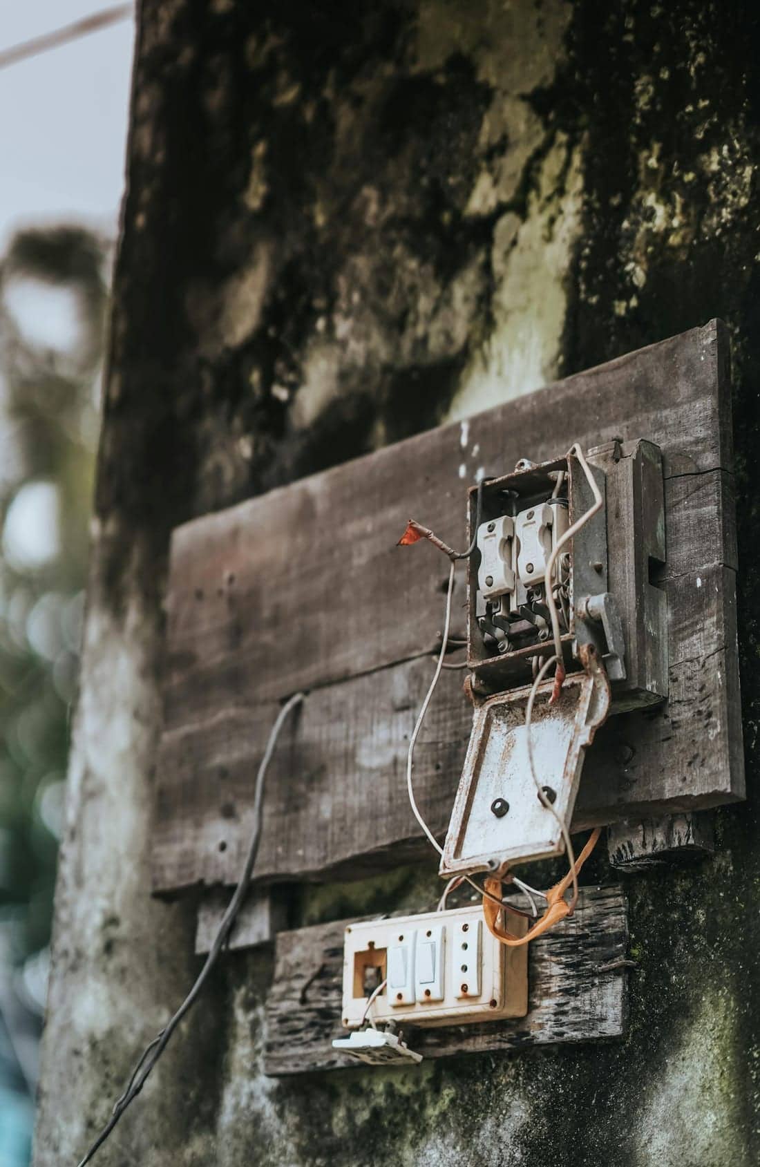 Weathered, aged electrical panel on a mossy wall in Nagpur, India - typical degraded installation with high electrical fire risk