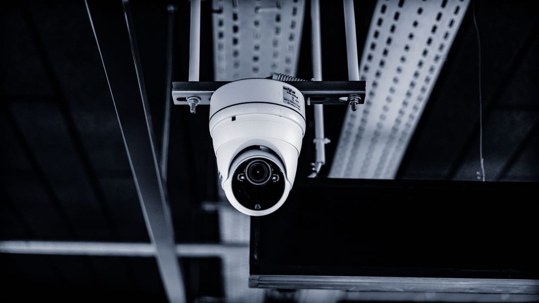 Technician servicing a wall-mounted CCTV camera - lens cleaning, connector inspection and aim verification during a scheduled AMC visit