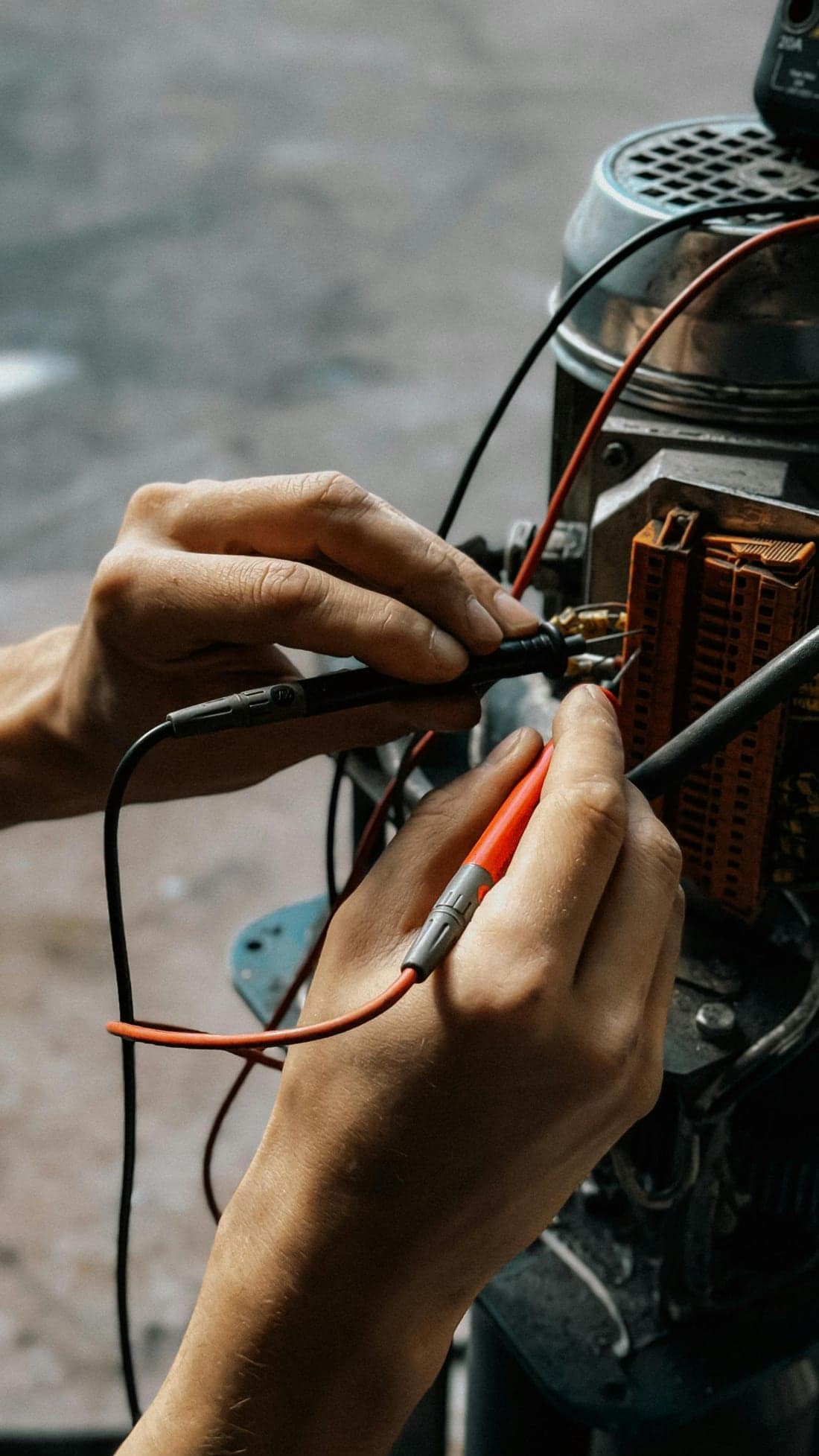 Close-up of hands using a multimeter to test continuity on motor wires - verifying earth continuity from equipment body to earth bus