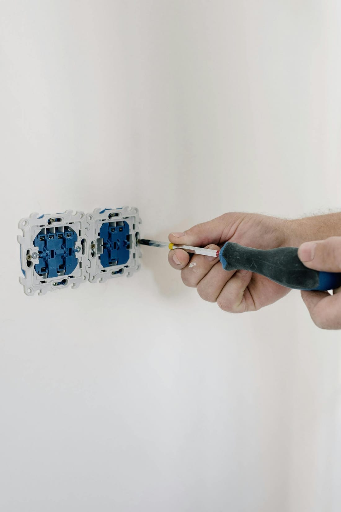 Electrician installing a wall switch with a screwdriver during a home electrical installation - typical residential switchboard work