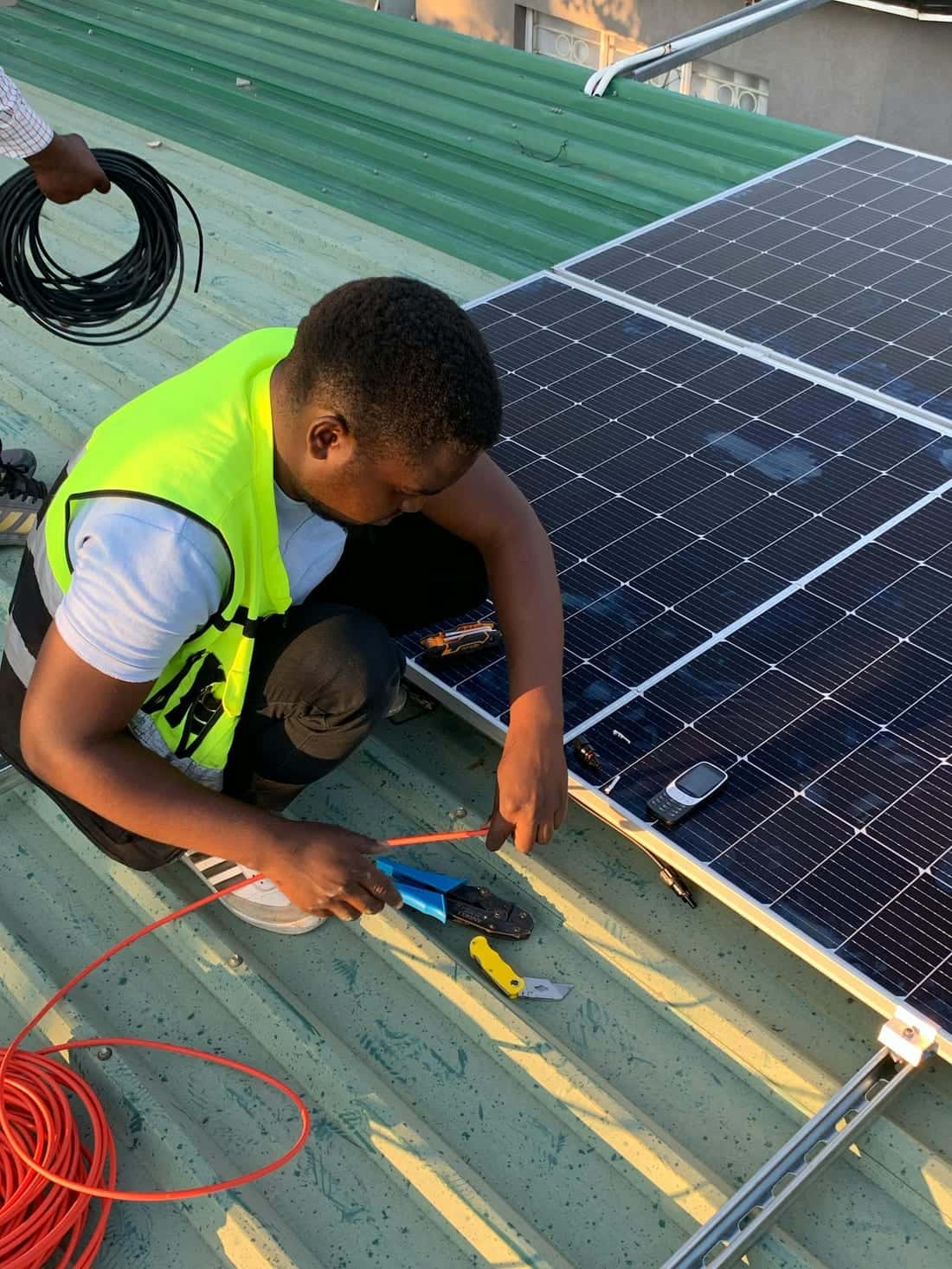 Technician working with cables and tools on a sunny rooftop during a solar system connection - DC cabling, earthing and inverter wiring