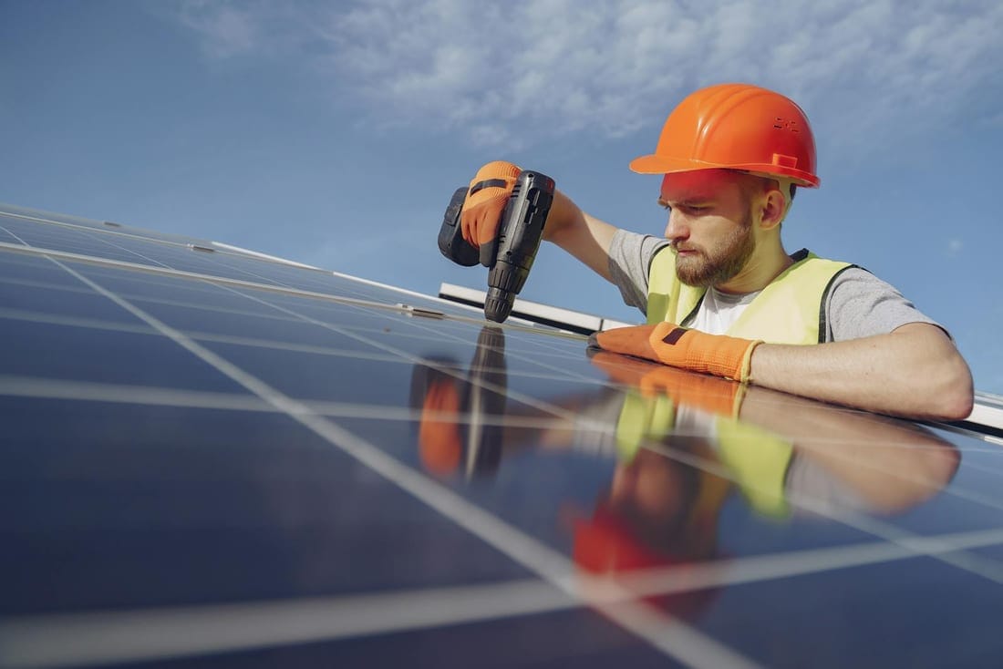 Electrician in a hardhat using a drill to mount a rooftop photovoltaic panel - structure and electrical work during a residential solar installation