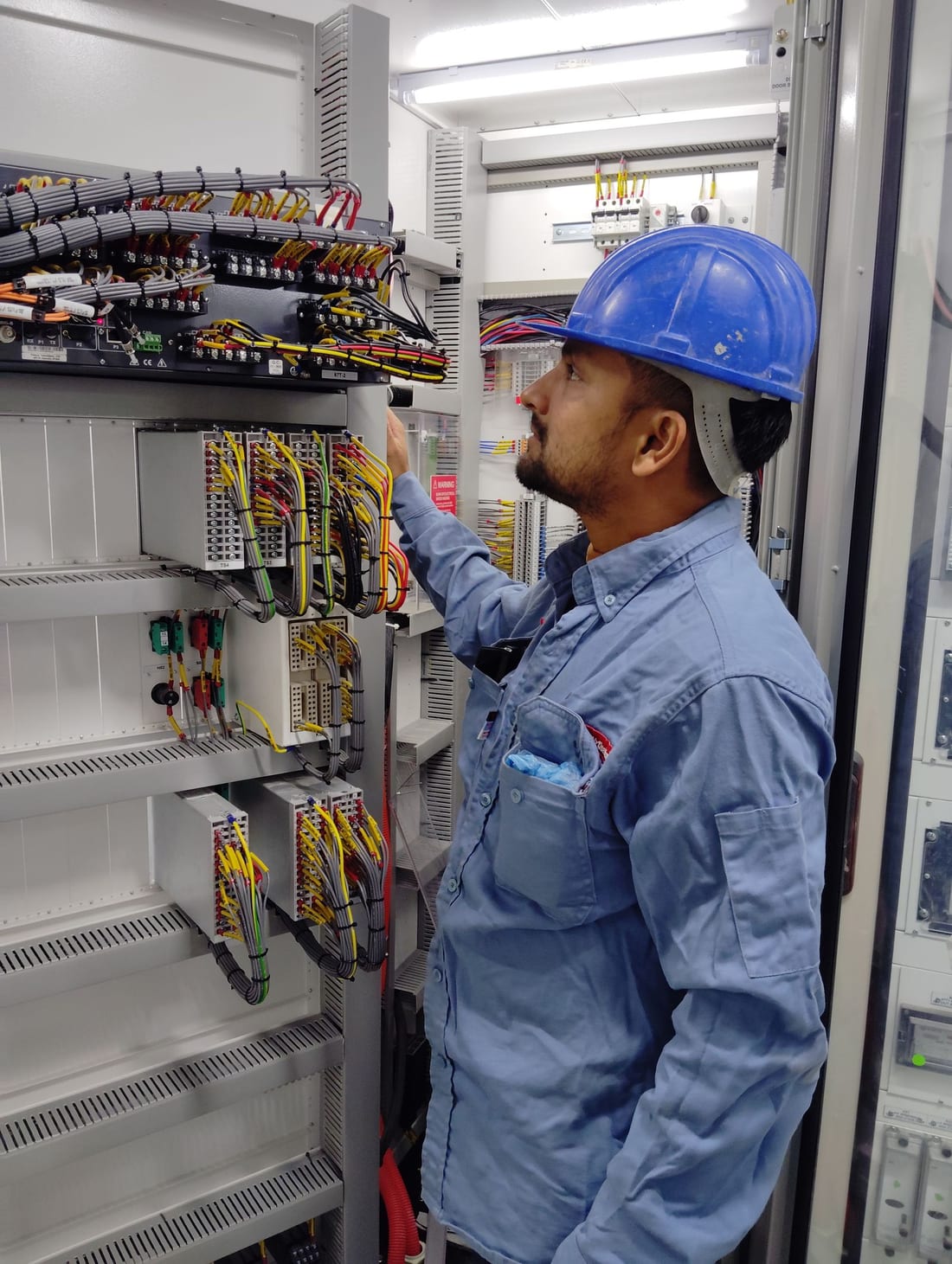 Electrician in a safety helmet carefully checking the internal wiring of an industrial distribution panel - panel installation and internal wiring verification